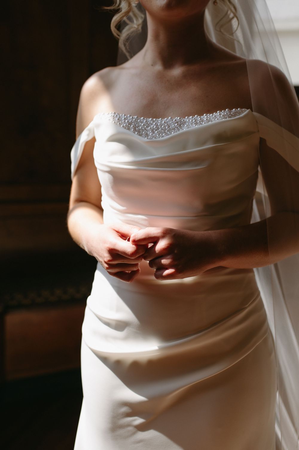 Elegant wedding dress detail showing beaded neckline and draped satin fabric in soft natural lighting.