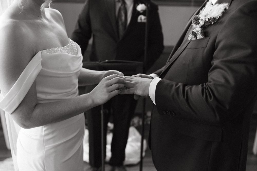A close-up black and white shot of wedding ring exchange during ceremony.