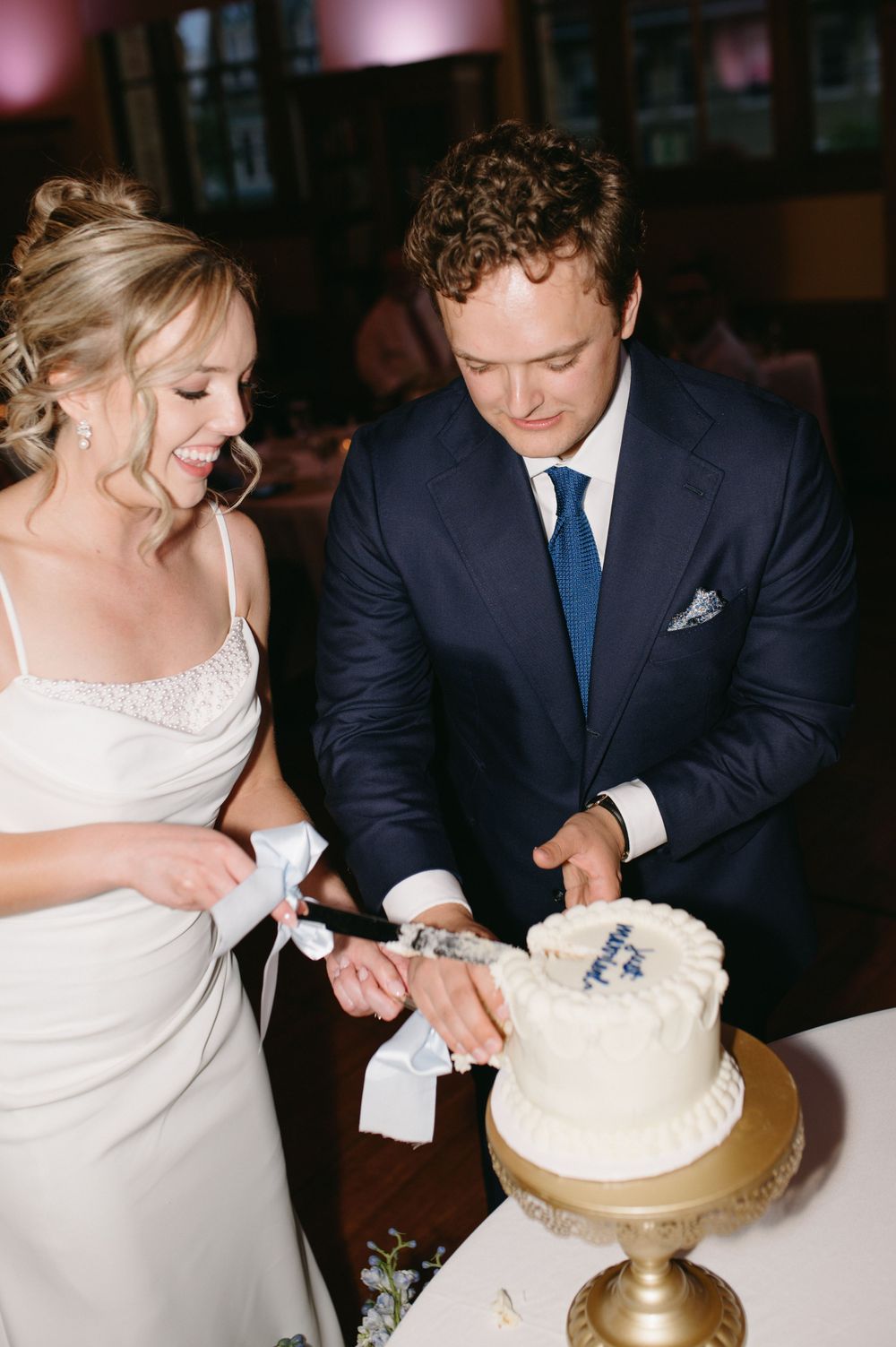 Couple sharing a joyful moment while cutting their white wedding cake together.