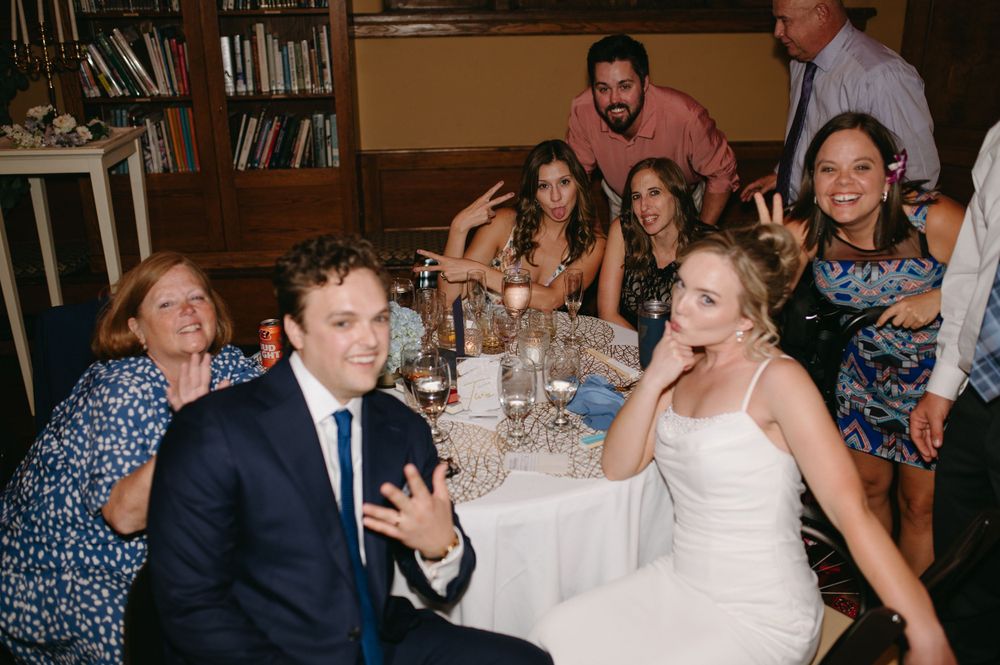 Wedding reception candid moment with guests laughing at decorated table.