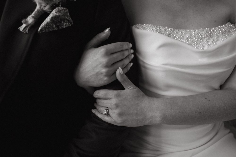 Close up detail shot of wedding couple's embrace showing dress fabric and ring.