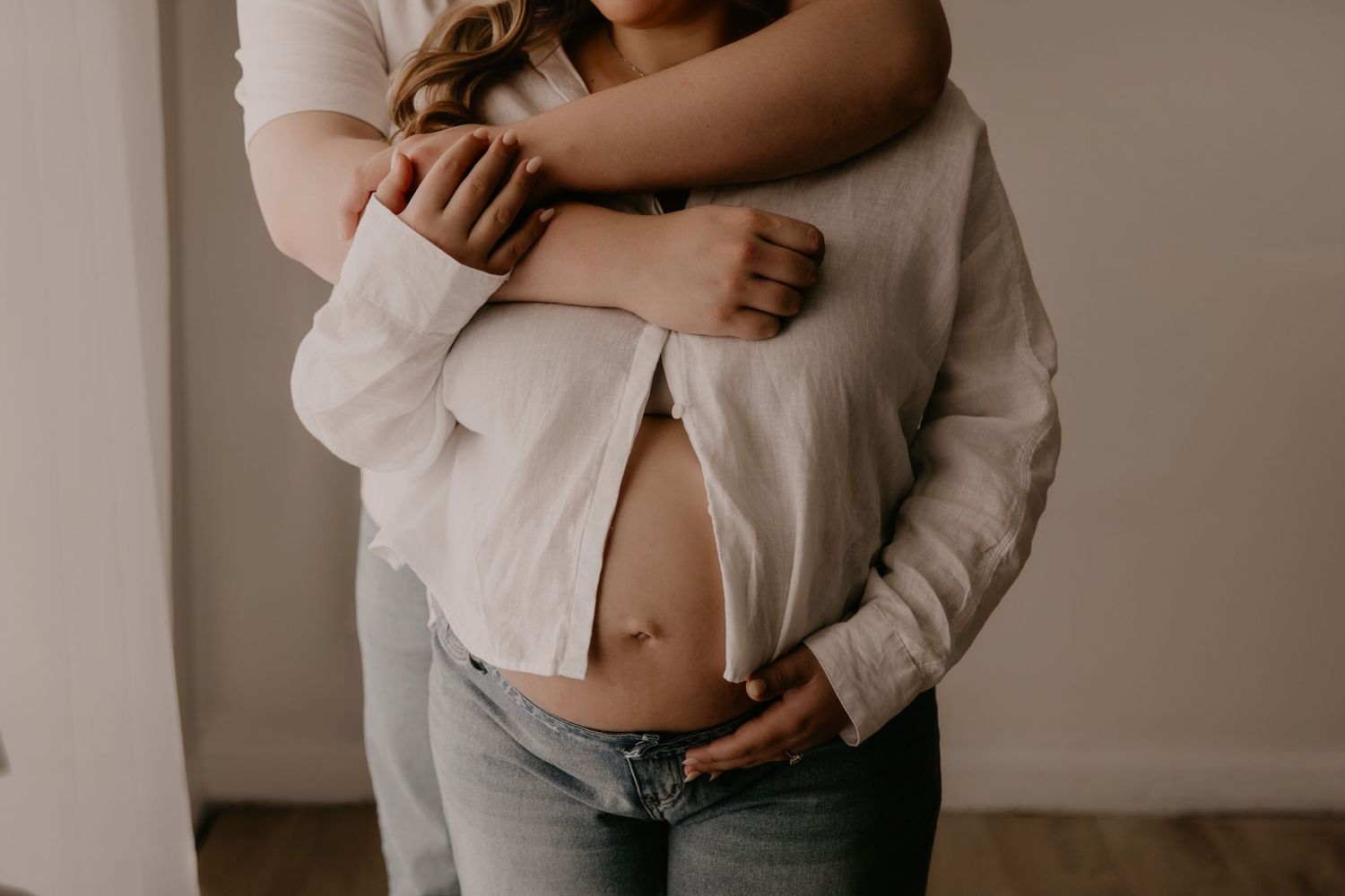 Couple embracing tenderly, showing pregnant belly in a soft, intimate maternity photo shoot.