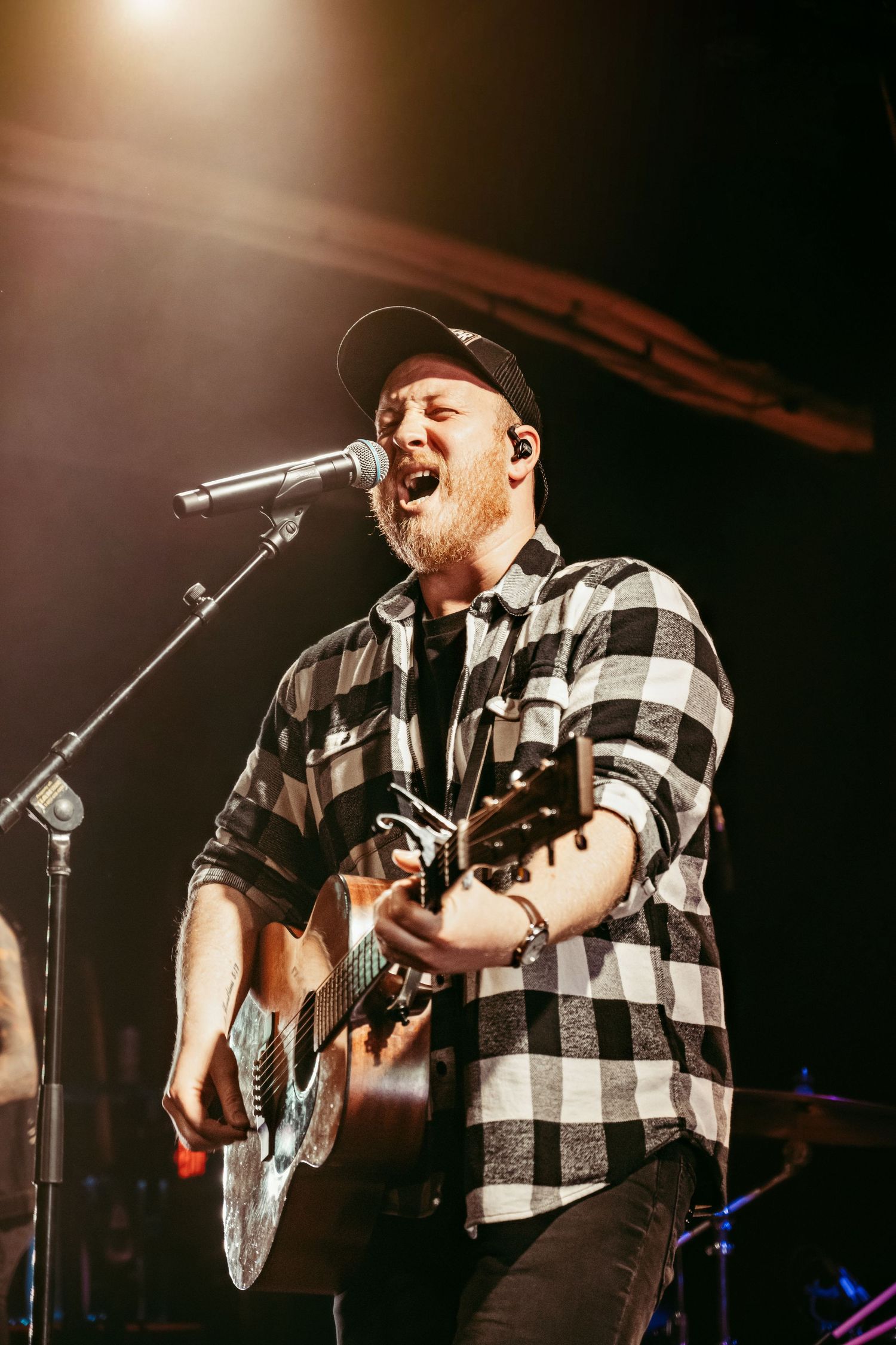 Passionate musician singing and playing acoustic guitar on illuminated stage.