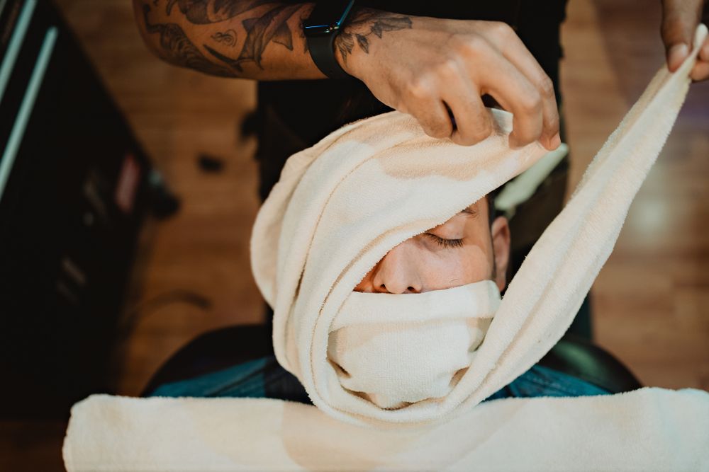 Groom’s face covered at the barbershop, prepping for the big day. Mazatlán wedding moments