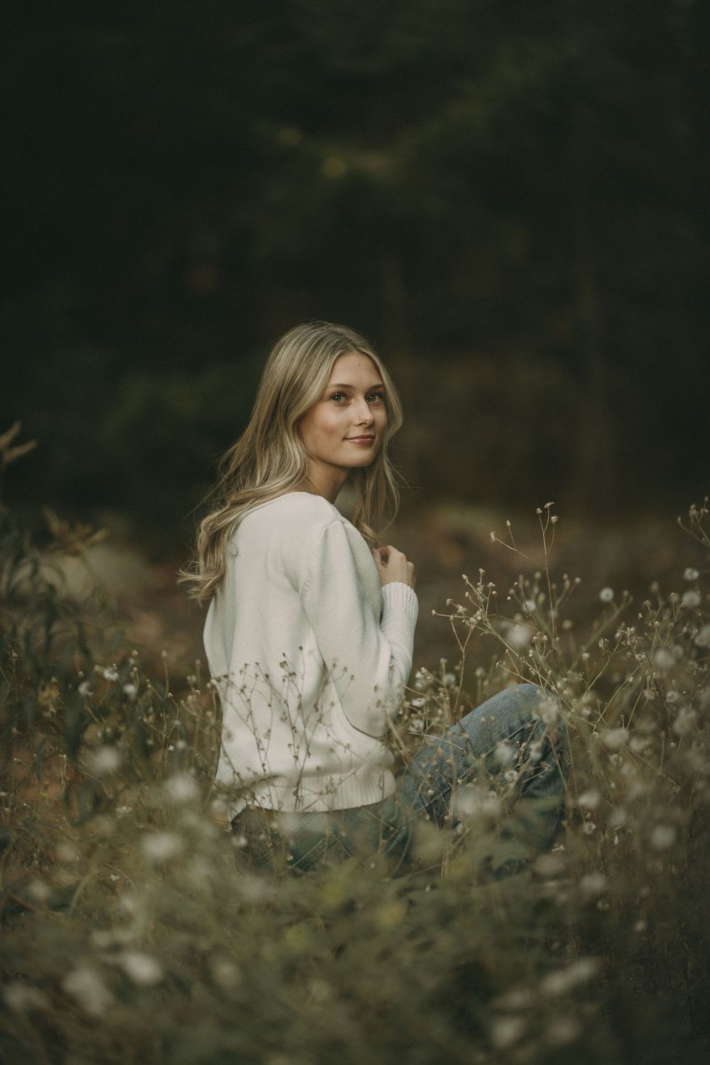 Moody outdoor portrait in dark tones with white sweater among wild grasses.