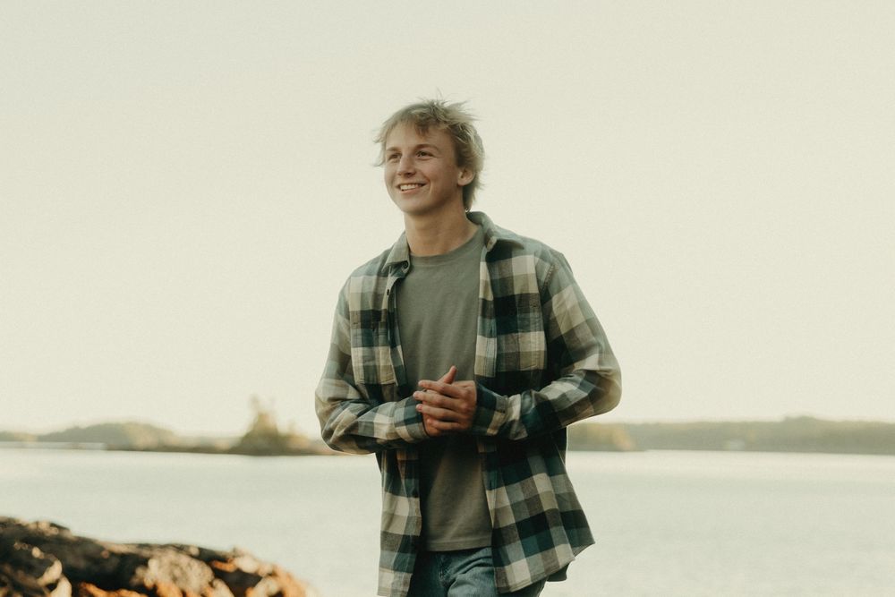 Person in plaid shirt stands by waterfront during golden hour photography session.