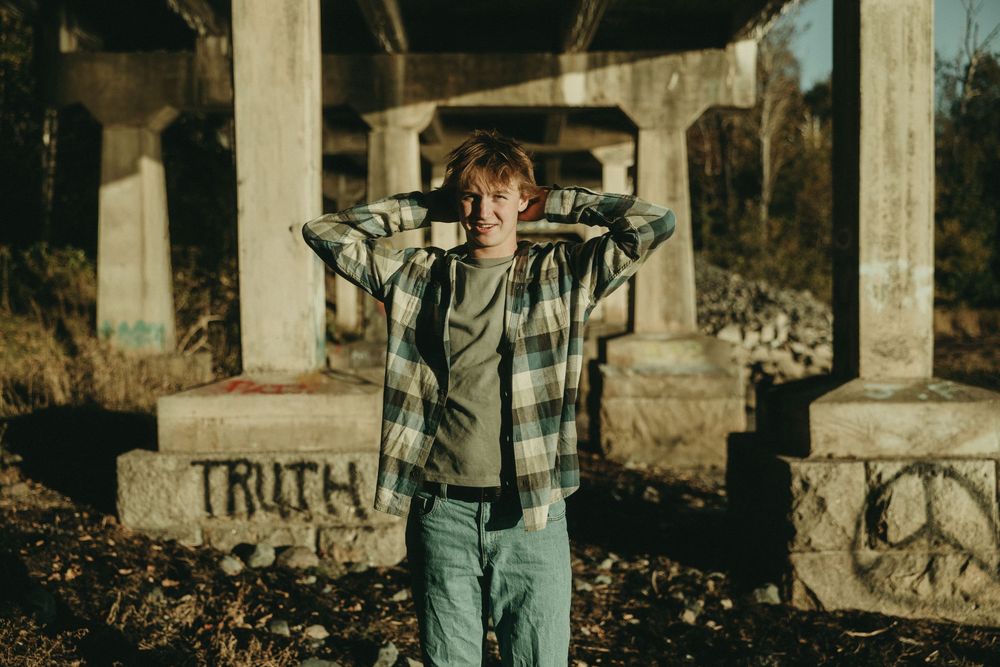 Individual poses near concrete pillars with graffiti in urban setting.