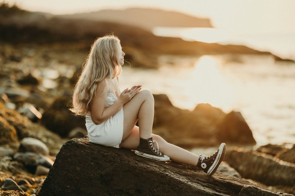 Person sitting casually on rocky coastal outcrop during golden hour.