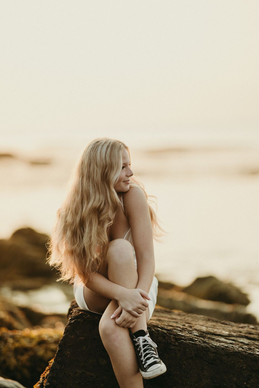 Lifestyle portrait session on rocky beach during warm sunset light.