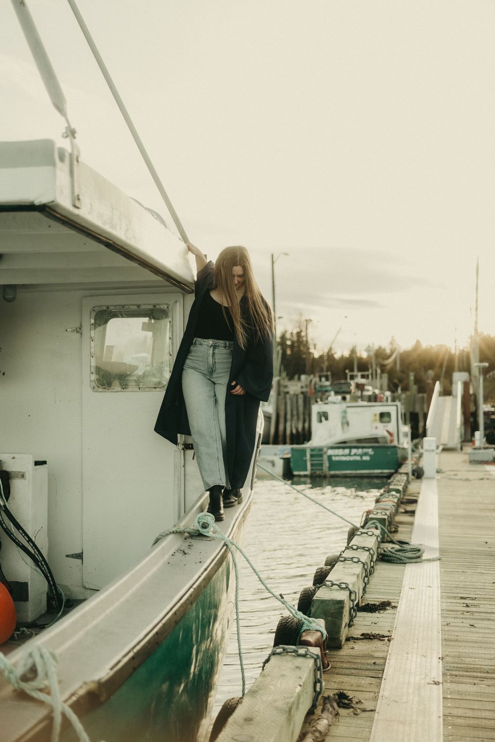 A person in dark clothing stands on a boat dock during golden hour.