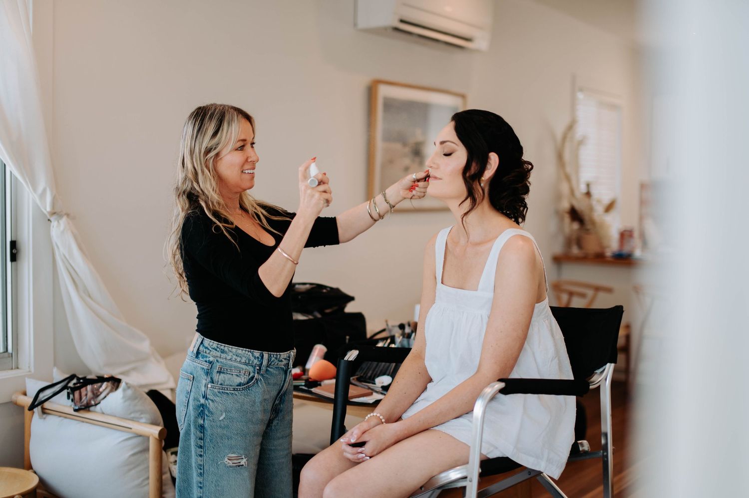 Bridal preparation scene showing makeup application in bright room.