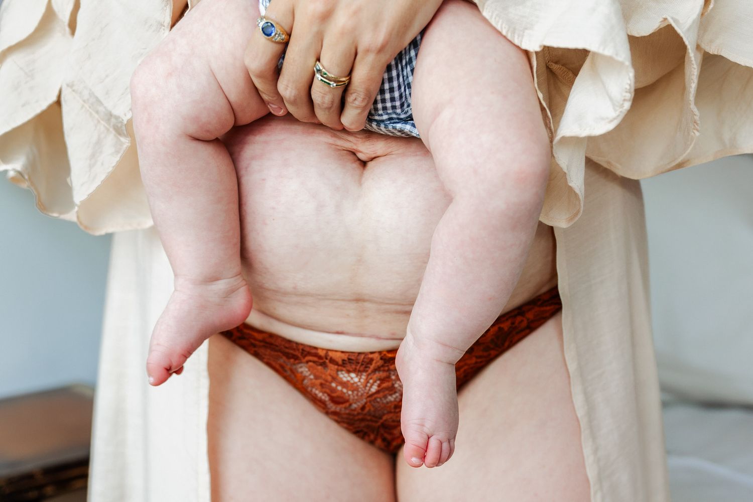 A postpartum mother holds her baby above her caesarean section scar at a Bristol newborn photographer photoshoot
