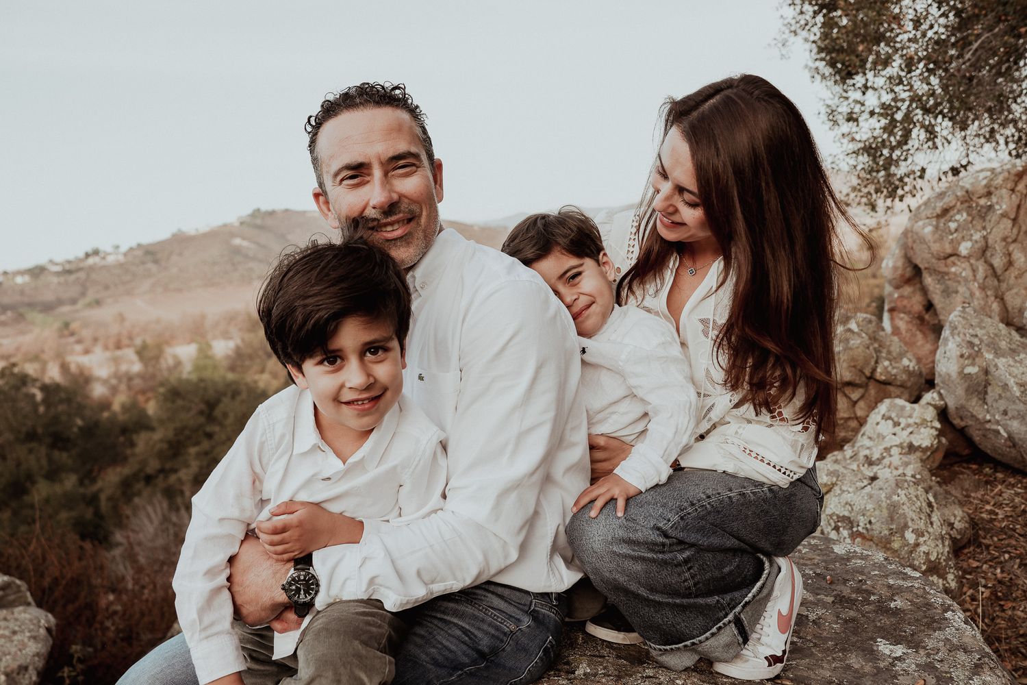 Happy family of four posing together on rocky mountain overlook.
