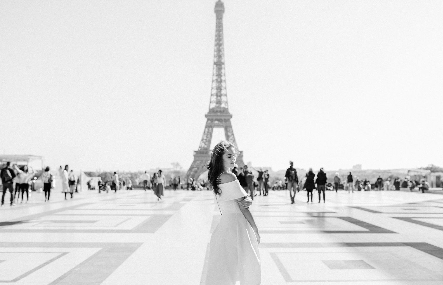 Black and white photograph of a person in flowy white dress at Trocadero Square facing the Eiffel Tower in Paris.