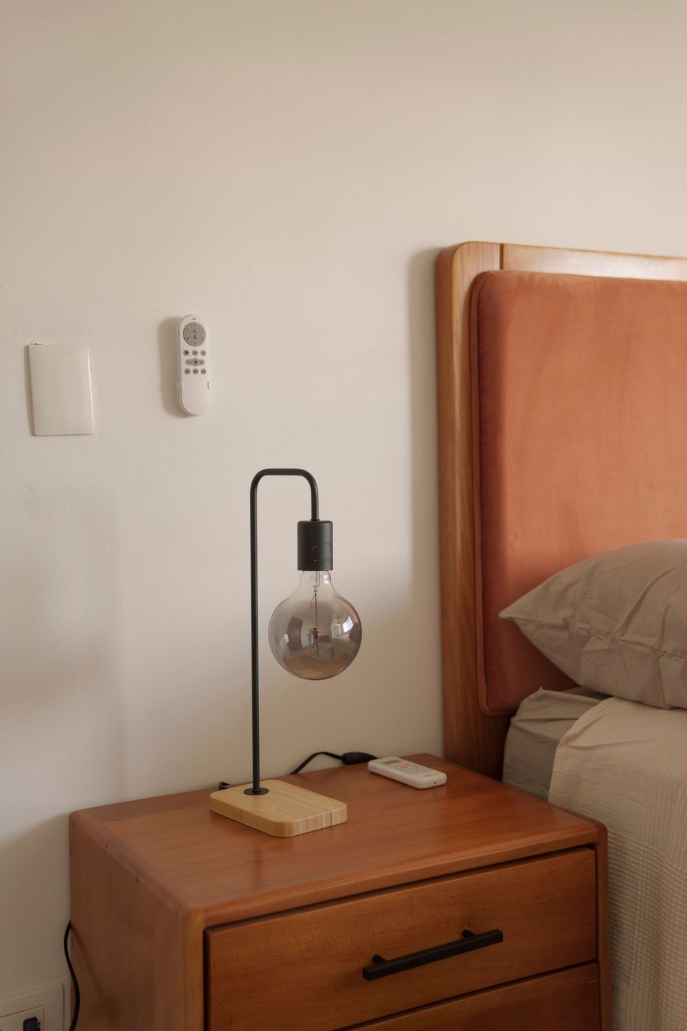 Contemporary bedside table with minimalist lamp and wooden headboard in warm tones.