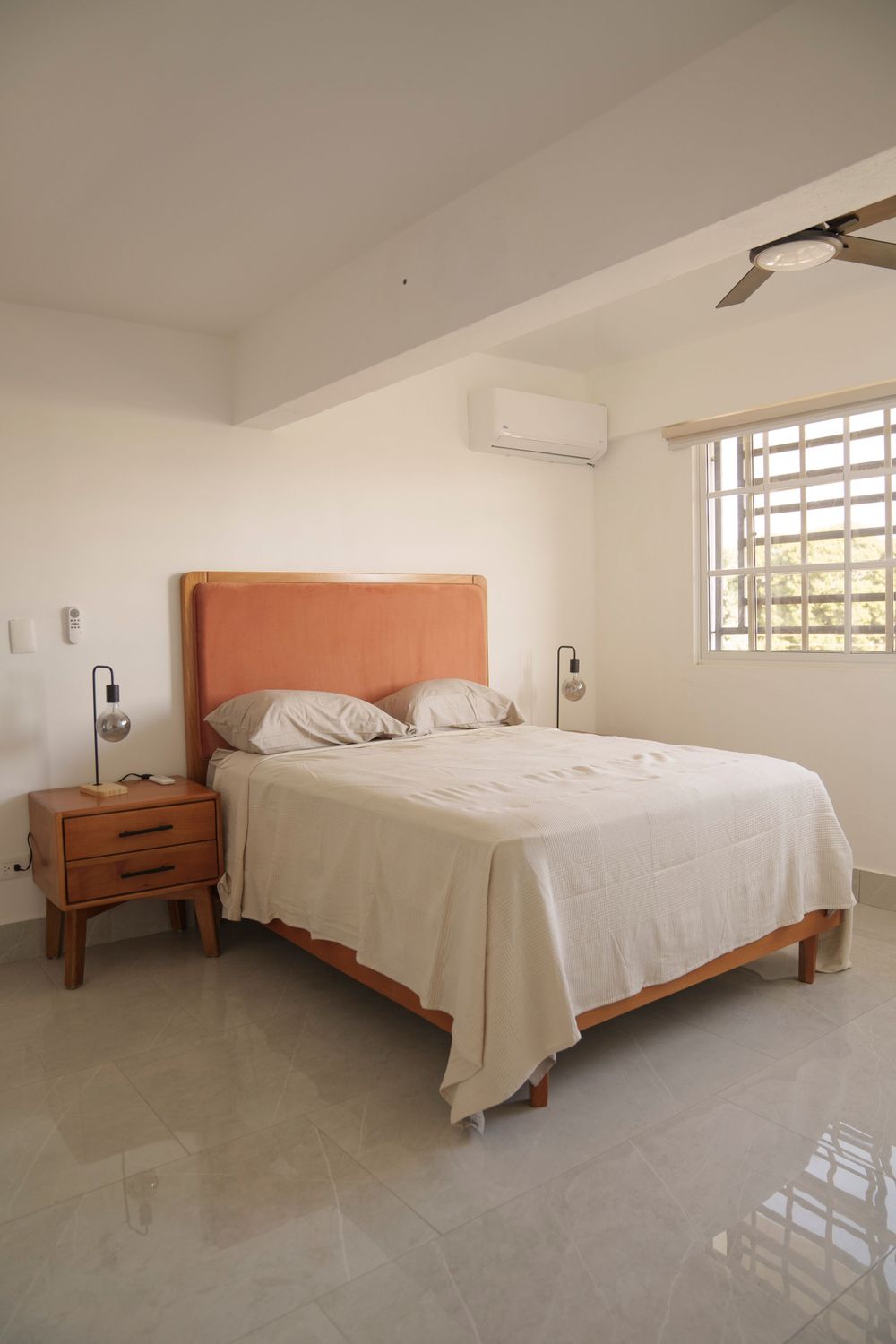 Minimalist bedroom with coral headboard, white bedding, and modern fixtures.