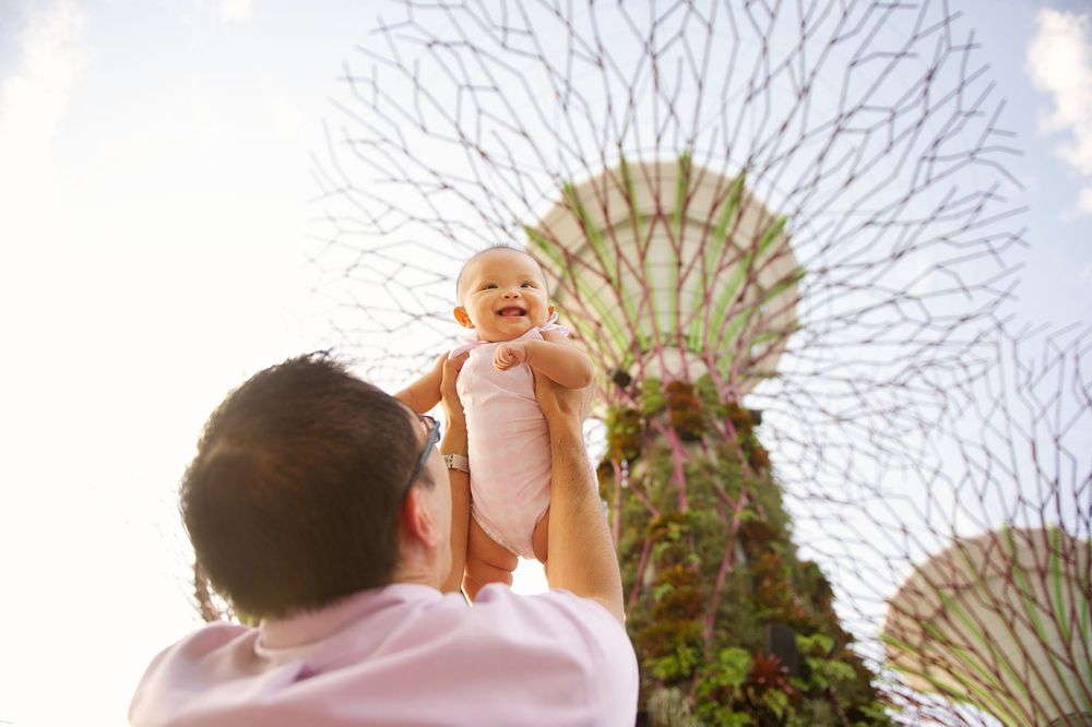 Dad holding his baby daughter up against a garden sculpture backdrop, taken by Phoebe Lee Photo in Toronto