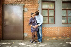 Expectant couple standing close against a brick building, with the father gently holding the mother's baby bump, photographed by Phoebe Lee