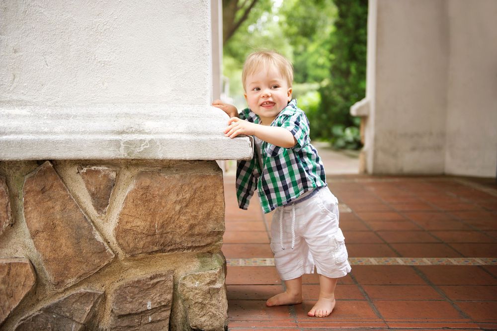 Barefoot toddler exploring a porch area by a stone wall, captured by Phoebe Lee Photo in Toronto