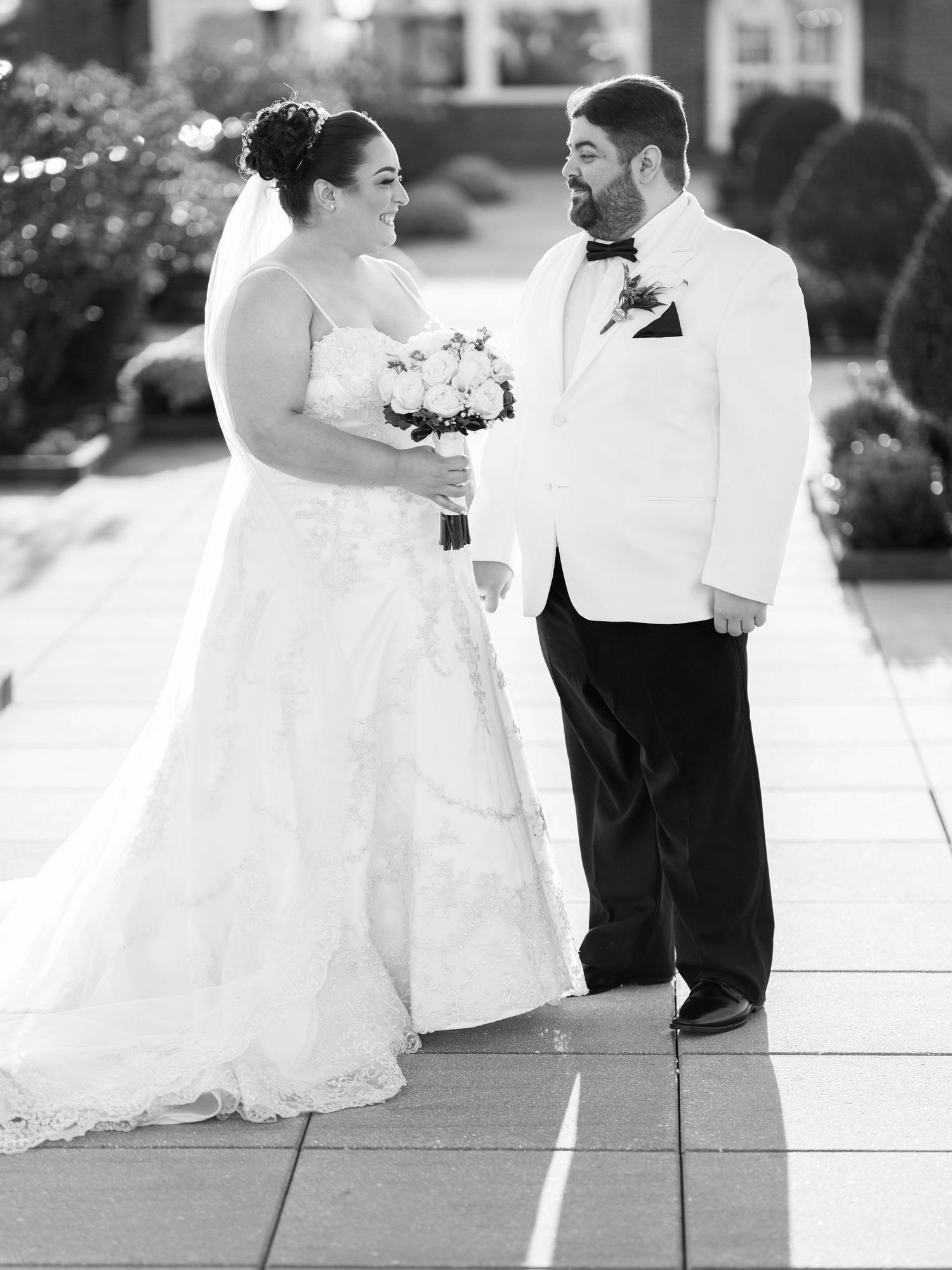 Black and white portrait of wedding couple in formal attire on outdoor walkway.