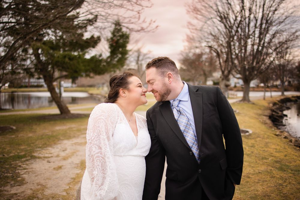 A couple in formal attire shares a romantic moment outdoors on a path during sunset.