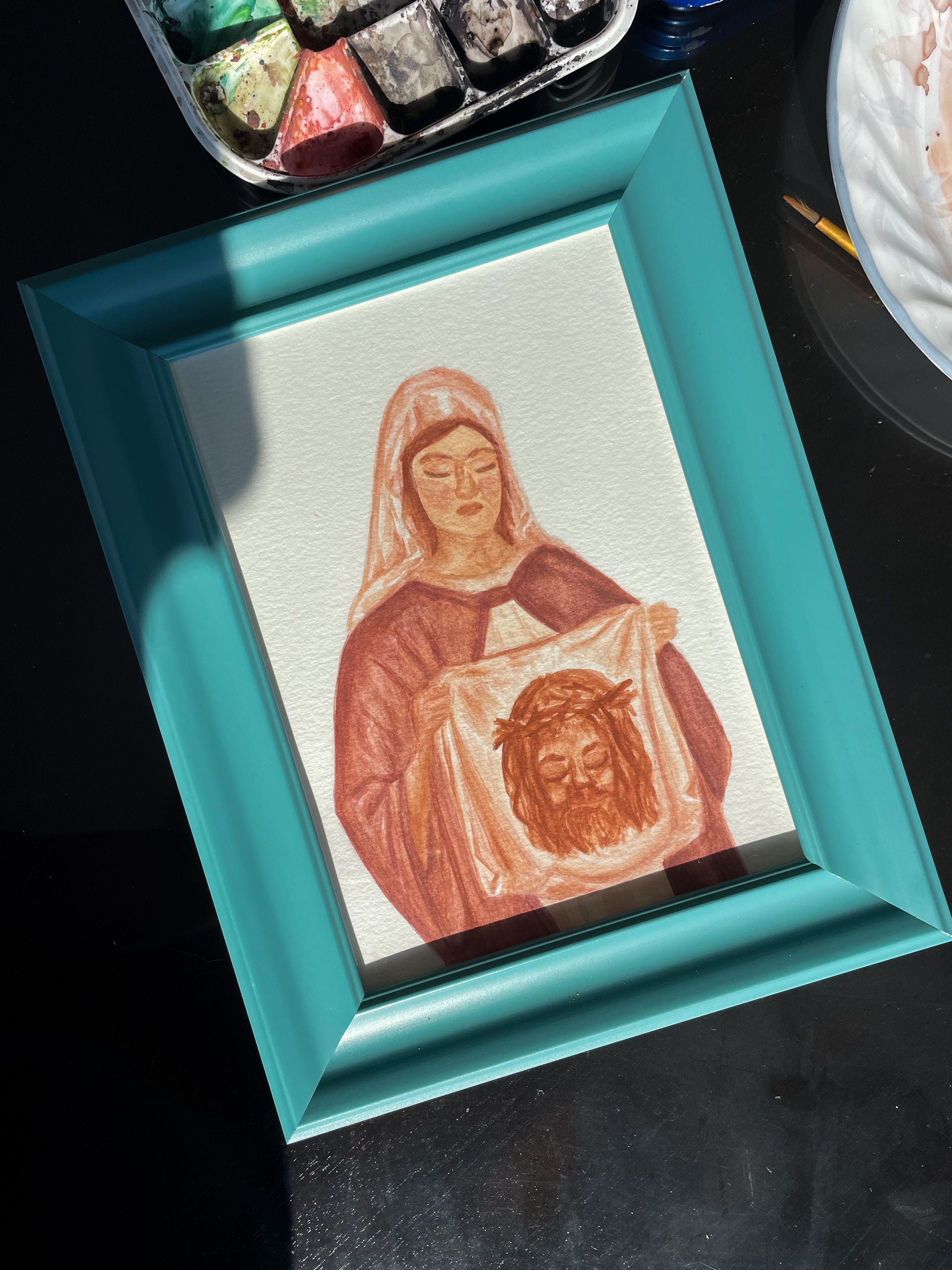 Watercolor painting in a turquoise frame showing religious imagery.
