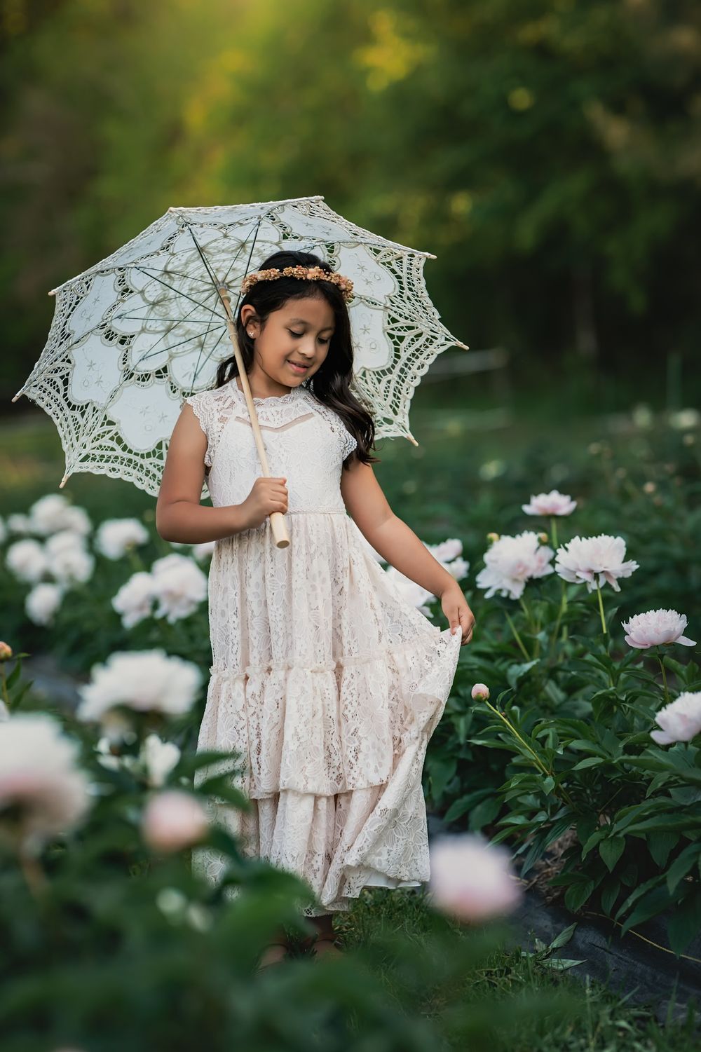 A dreamy garden portrait with white lace dress, parasol, and pink peonies creating an ethereal scene.
