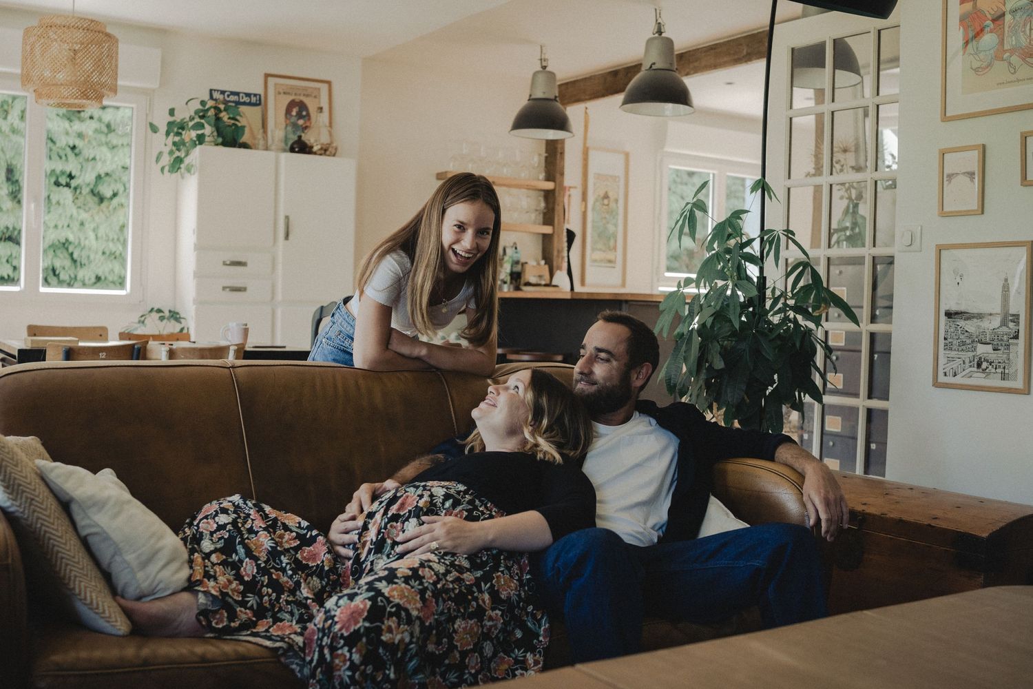 Famille se détendant ensemble sur un canapé confortable dans un salon lumineux, décoré de plantes et d’œuvres d’art.