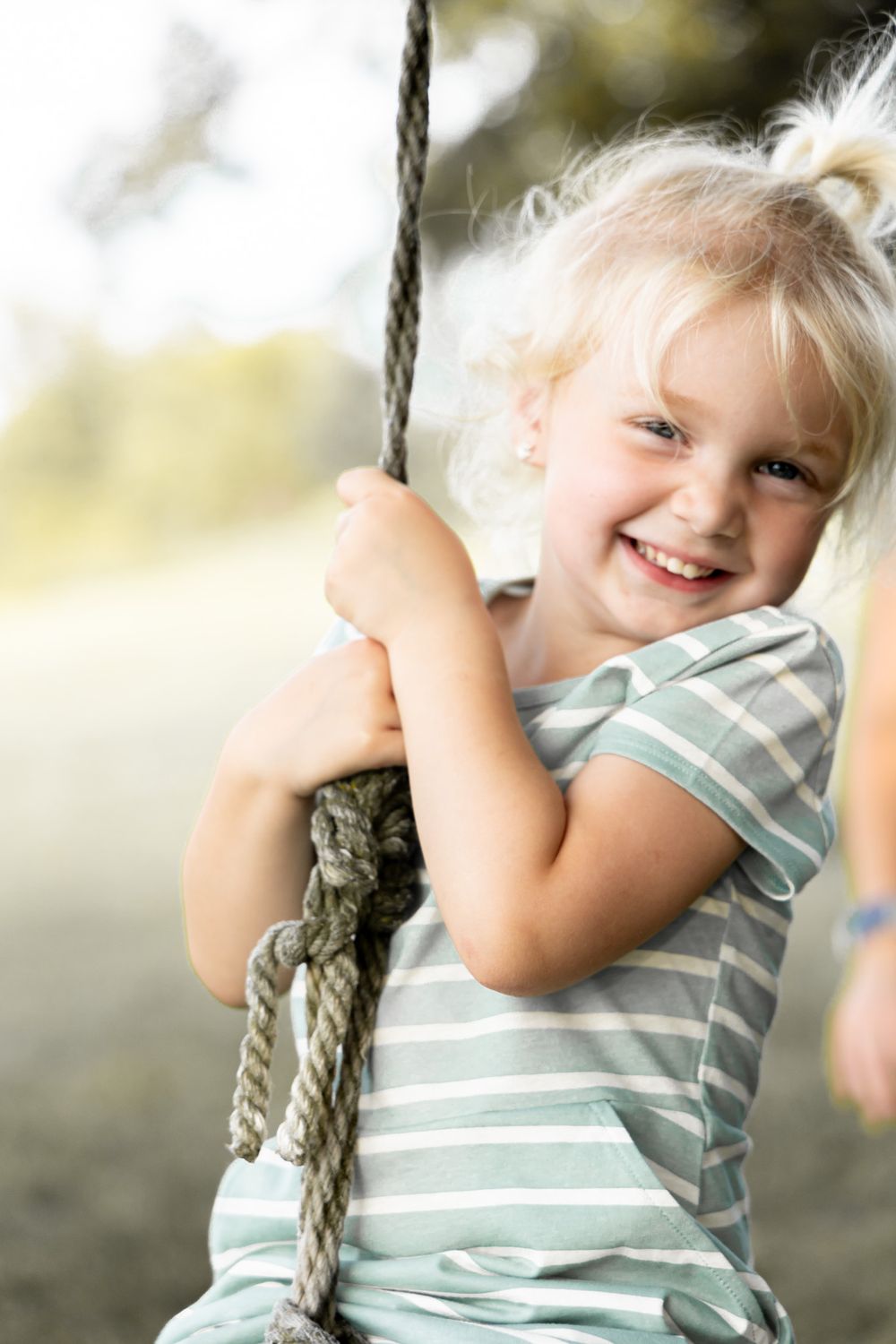 A young child in striped clothing swings joyfully on a rope swing outdoors.