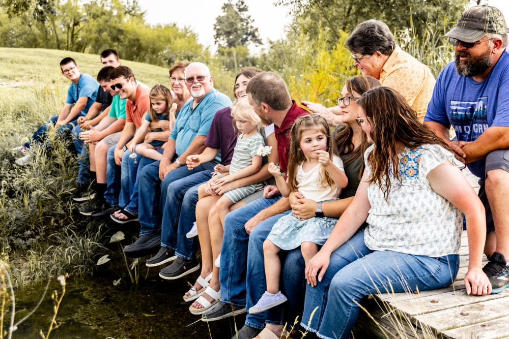 Large group sitting together on a wooden ledge outdoors during golden hour.