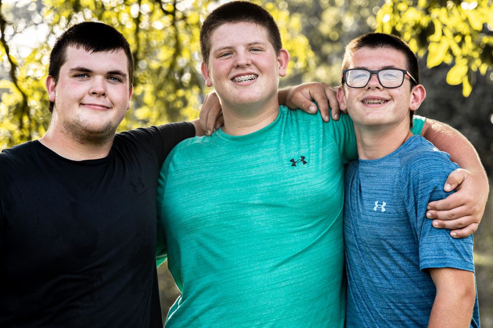 Three young people in athletic wear smiling and embracing outdoors.