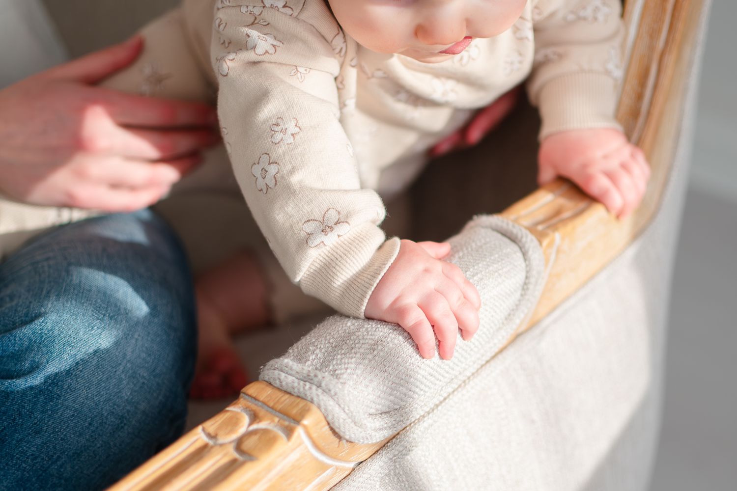 Small hand touching wooden handrail while wearing cream colored long sleeve shirt and grey socks.