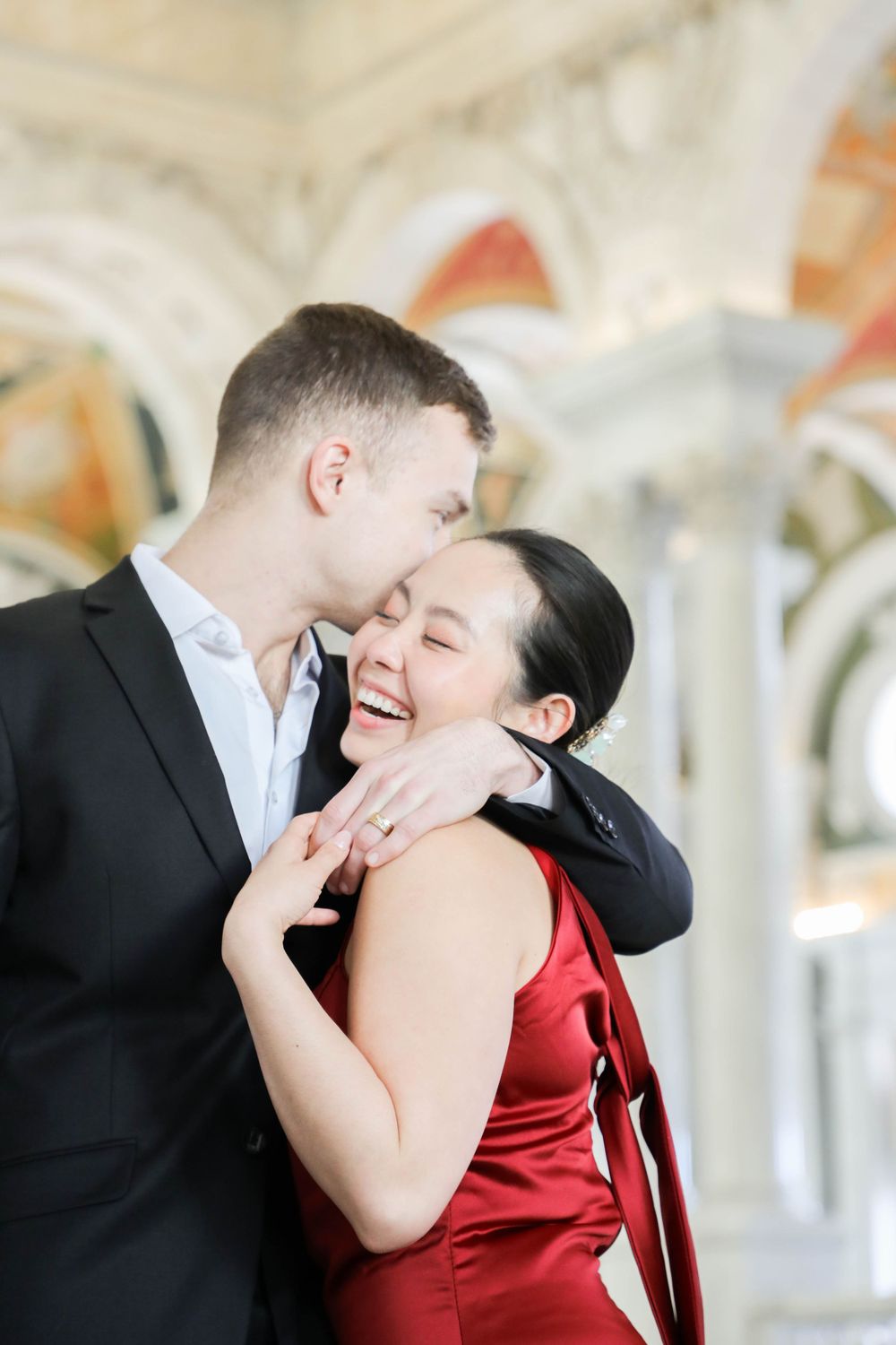 A couple shares a tender romantic moment together, with her in a red dress and him in a black suit.