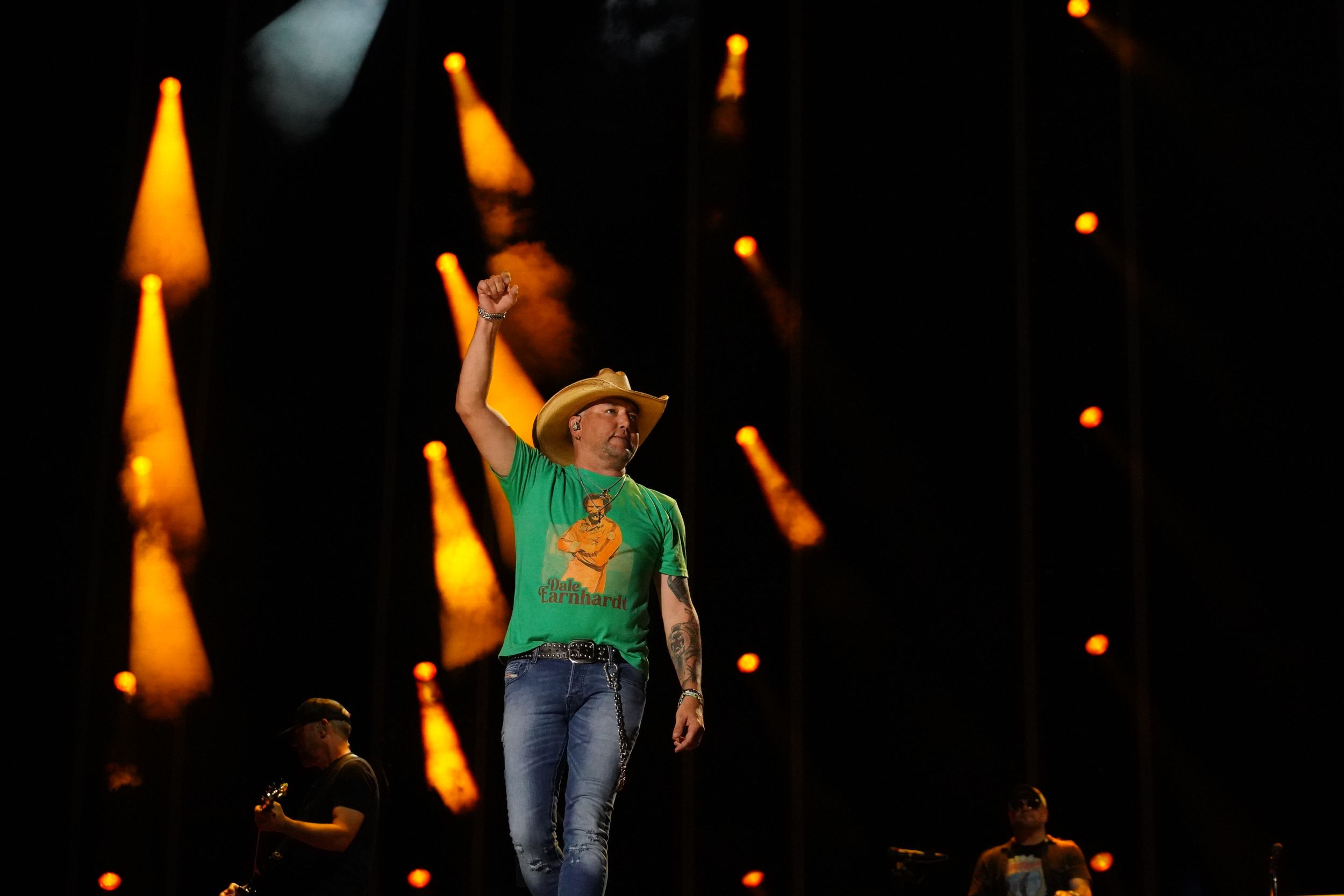 Concert performance with warm orange stage lighting and performers in casual attire.
