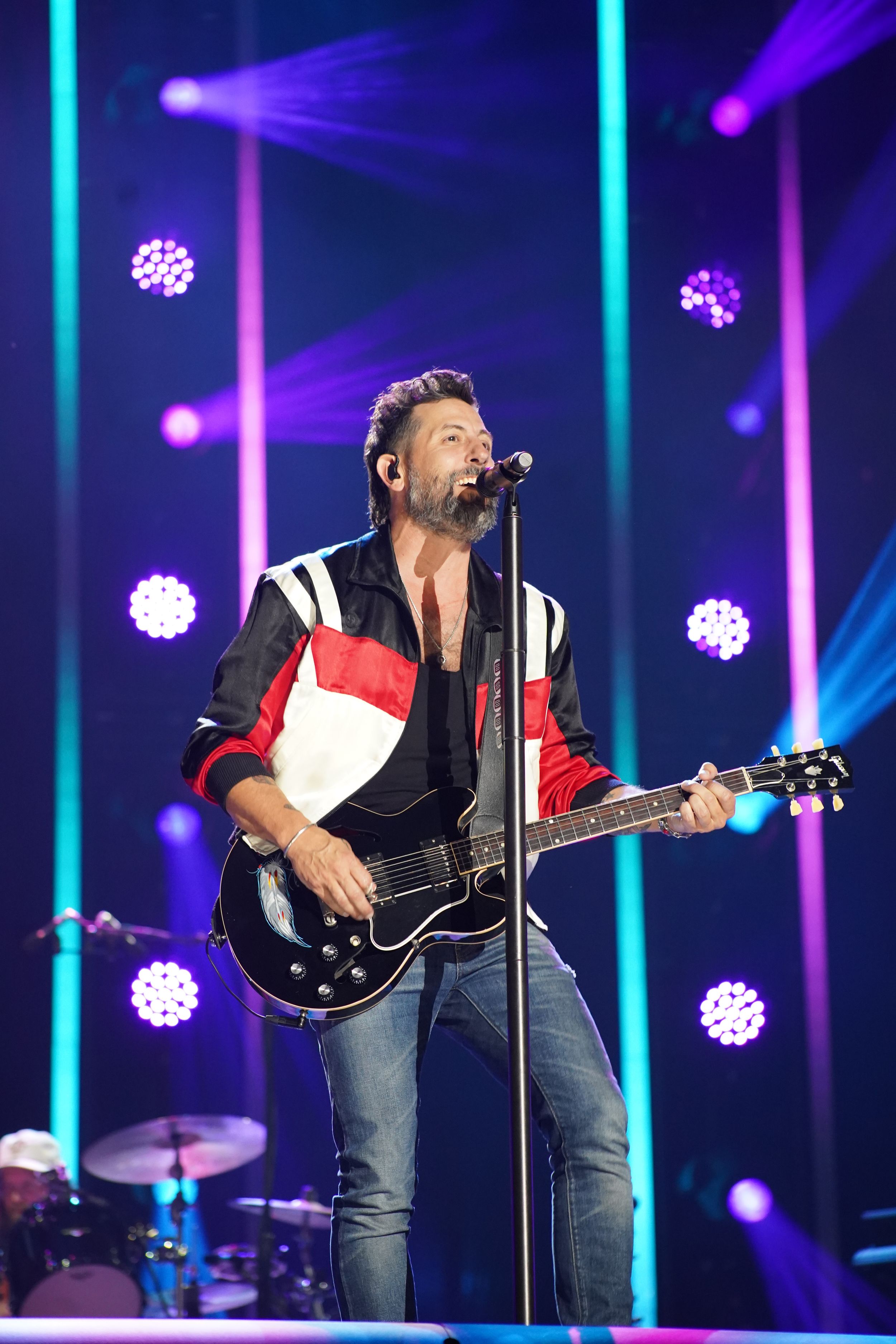 Concert stage with dramatic purple and blue lighting featuring guitarist in denim.