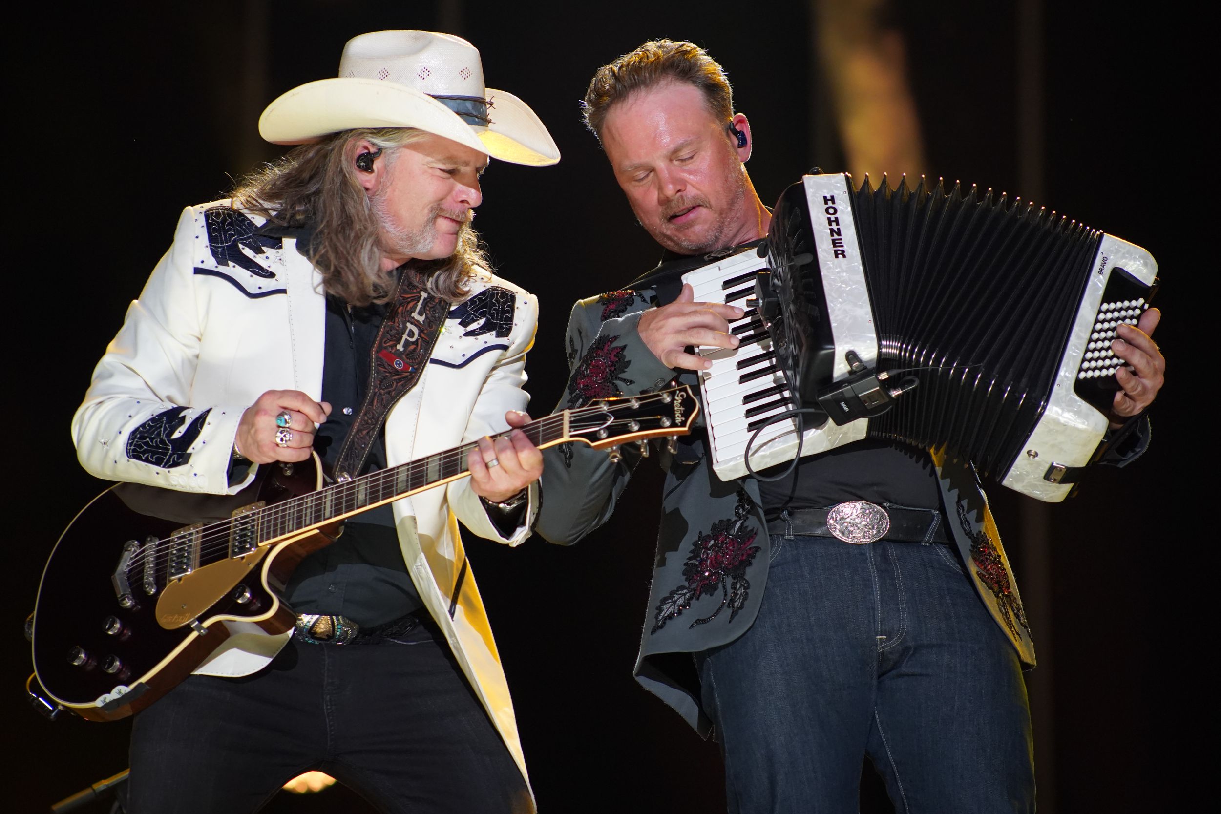 Musicians in cowboy hats performing with guitars and accordion on dark stage.
