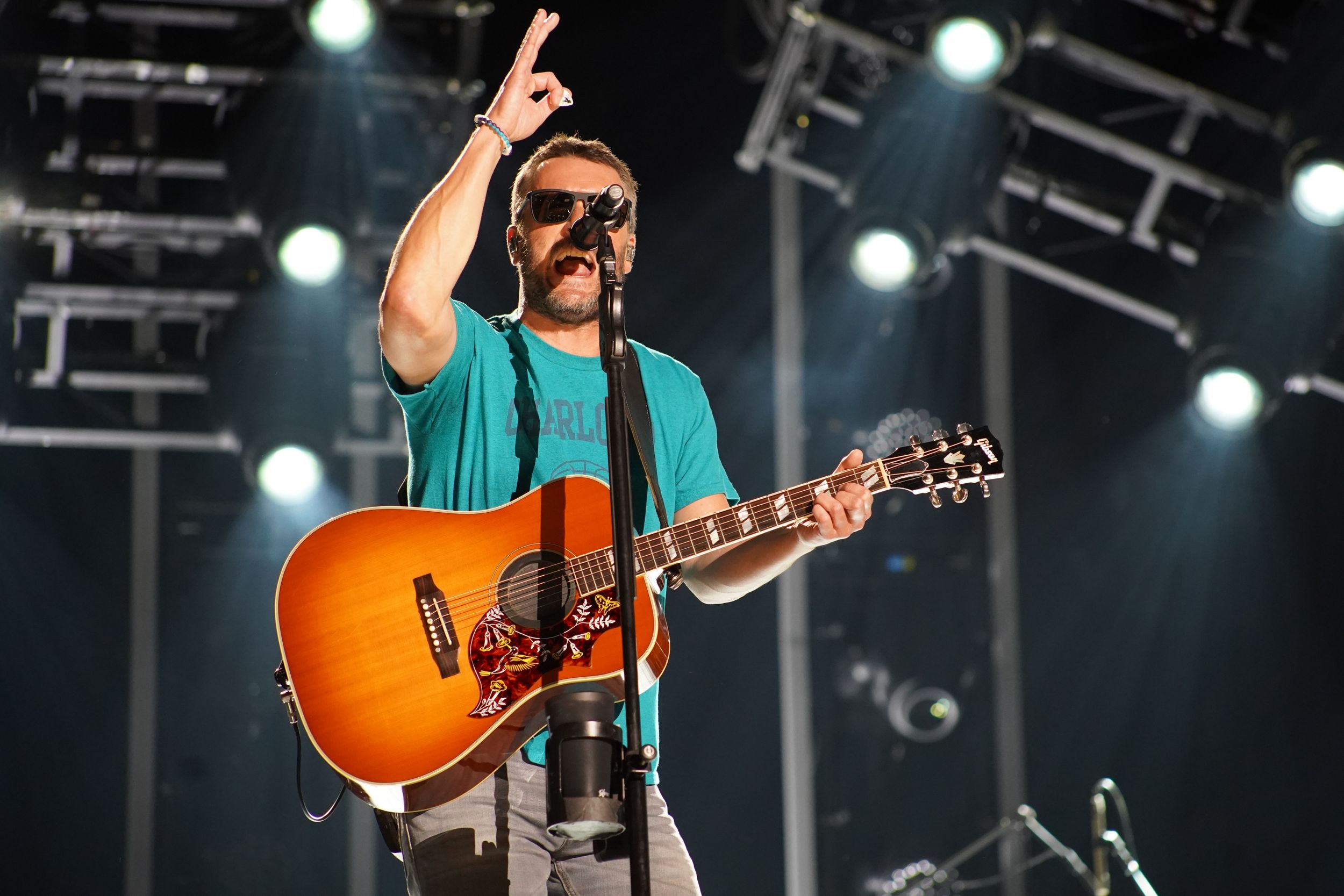 Country musician performs on stage with sunburst guitar under bright concert lighting.