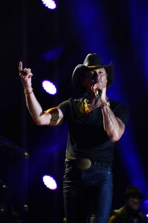 Stage performer in dark clothing and cowboy hat silhouetted against blue concert lighting.