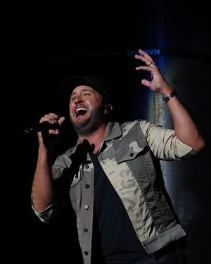 Concert performer in vest gesturing dramatically on dimly lit stage.