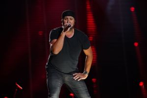 Stage performer in dark attire singing passionately during a dramatic concert performance.