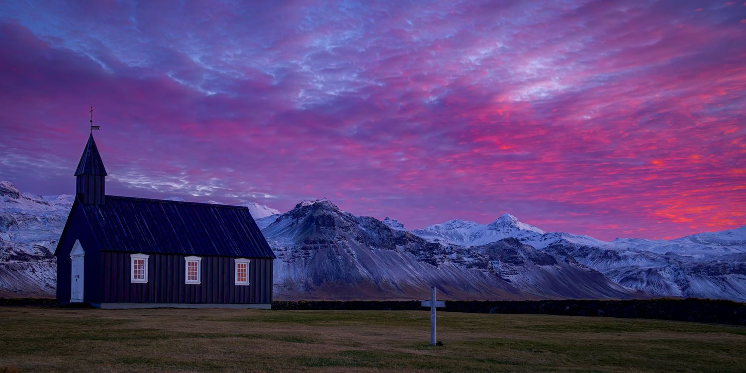 pink hues fill the sky at sunrise at the black church at Budir in Iceland