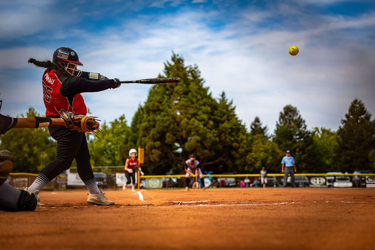 Softball batter in red uniform swinging at a ball during a daytime game.