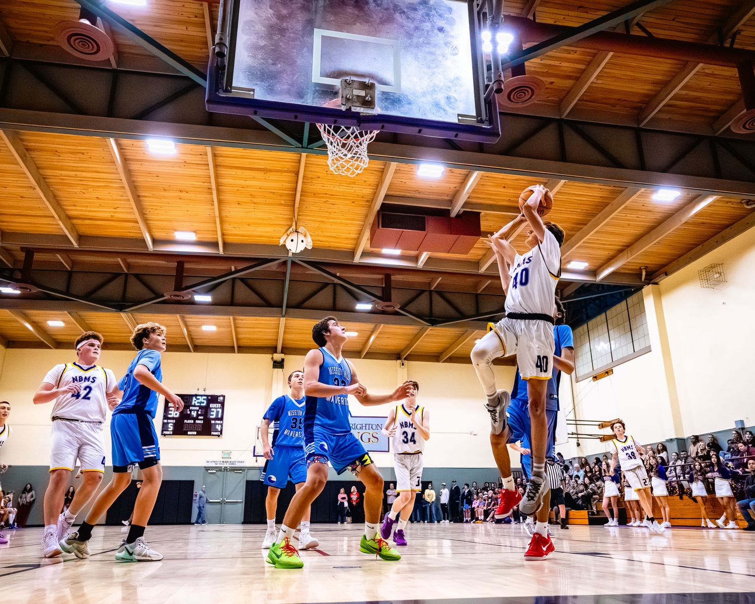 Basketball players competing for a rebound under the hoop in an indoor gymnasium.