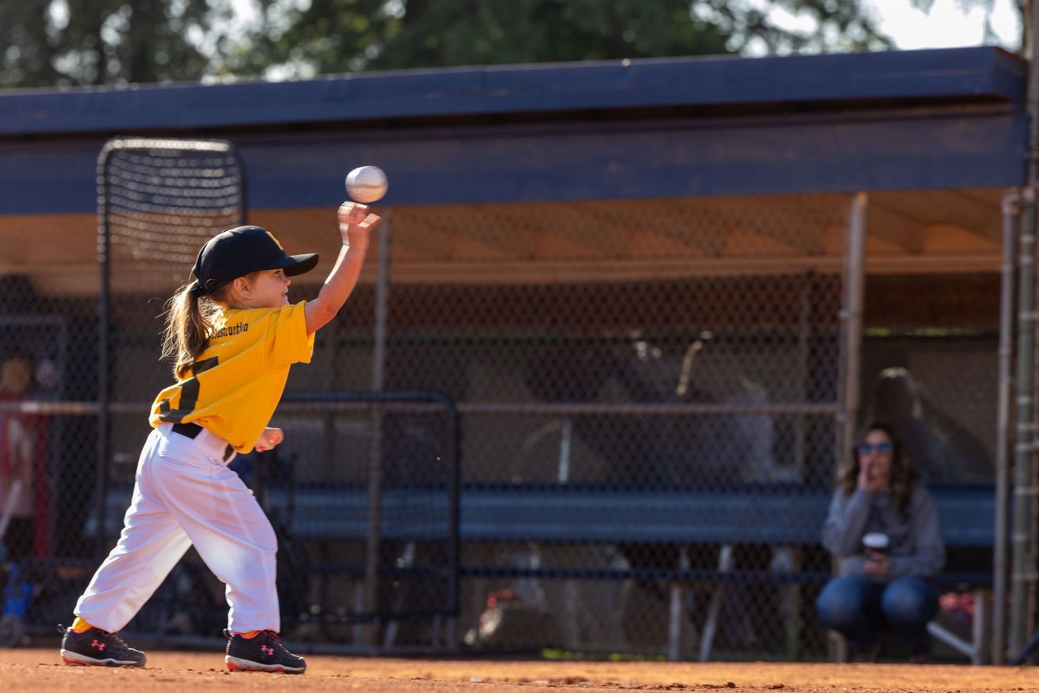 Youth baseball player in yellow jersey pitching ball during sunset game.