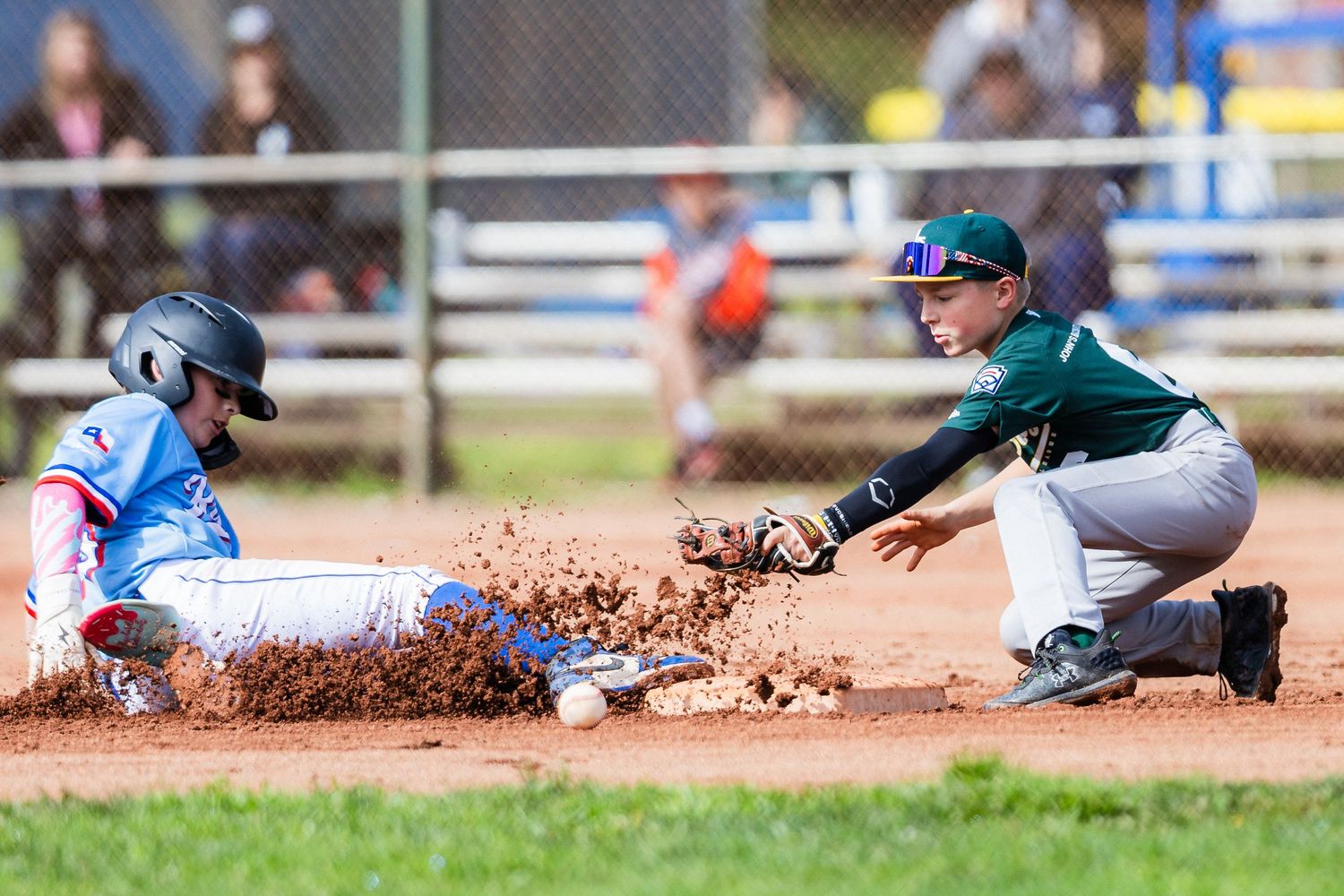 Baseball players create dust cloud during dramatic sliding play at base.