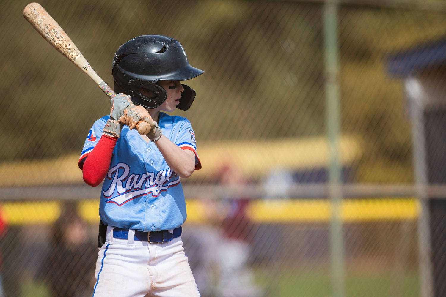 Young baseball player at bat in light blue uniform takes batting stance during youth baseball game.