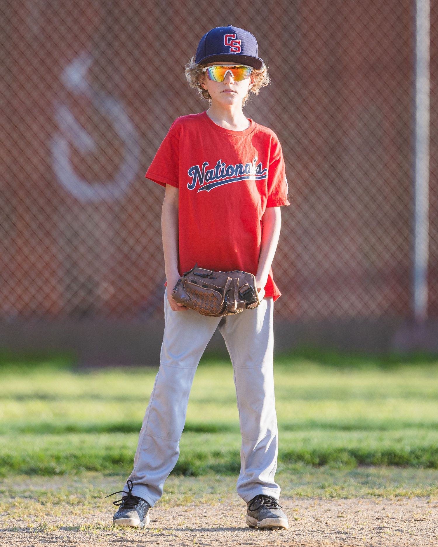 Young baseball player in red Nationals jersey stands ready on field with glove.
