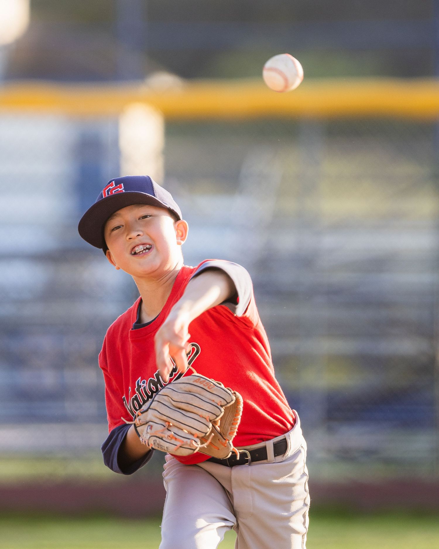Young baseball pitcher in red uniform throws ball during game.