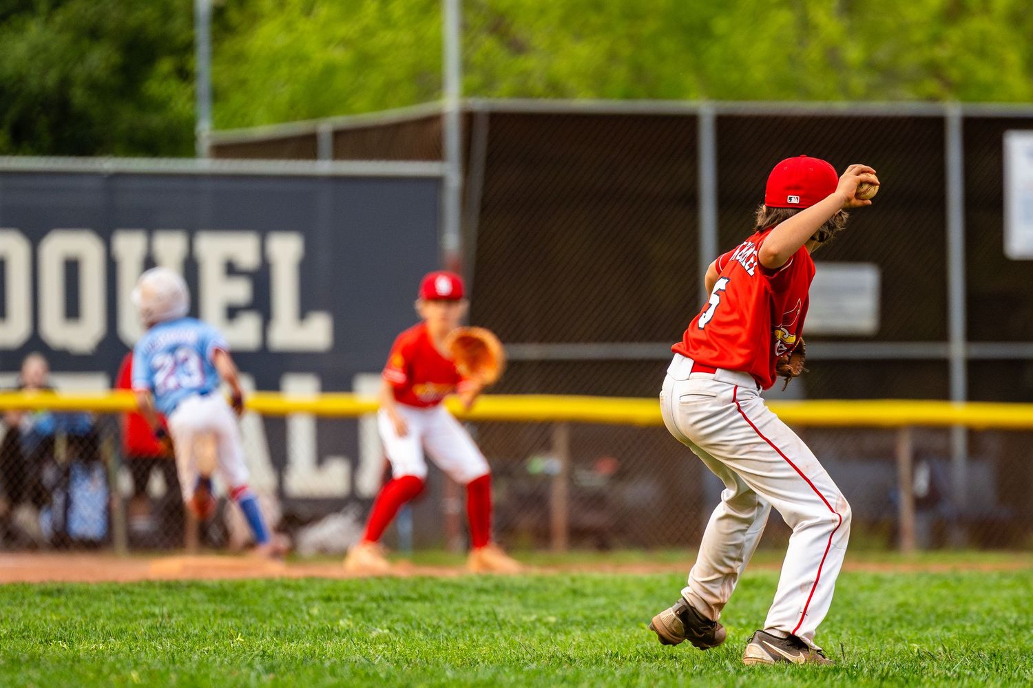 Youth baseball player in red uniform fields a ground ball during a game.