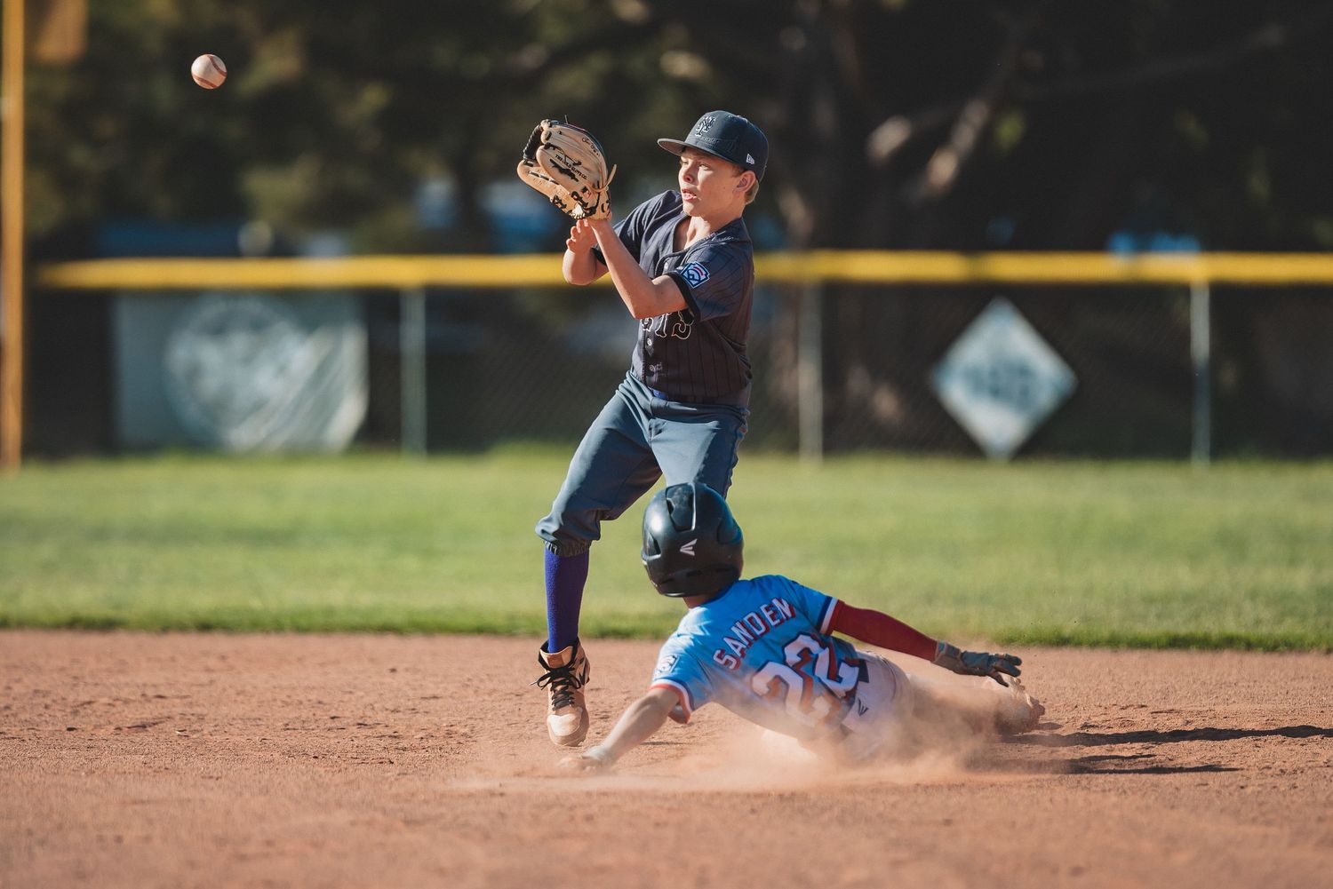 A baseball player leaps to make a throw at second base while a sliding runner attempts to steal the base.